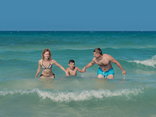 Family of three people getting out from sea water together. They smiling and  enjoying thier summere vacations. Front view.