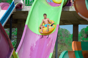 Summer fun in water park. Cute boy sliding down slide on colorful inflatable floater.  He is on his...