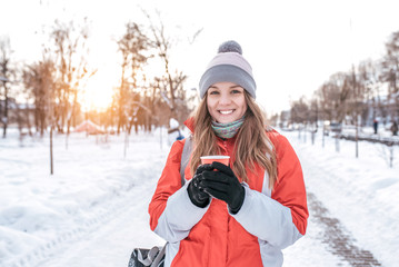 Fototapeta na wymiar happy girl winter street in city smiling and laughing, holding cup tea with hot drink, coffee warming cold winter day. Camping weekend, free space text. Warm jacket hat gloves, emotions pleasure .