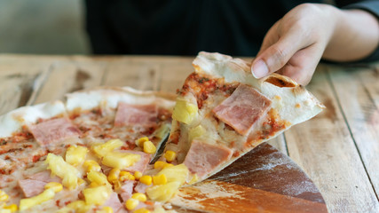 Hands taking slices of homemade Italian pizza on a wooden table.