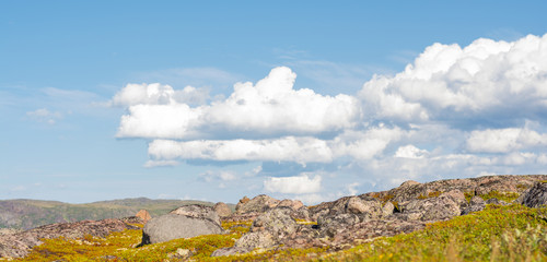 Huge rounded stones on backdrop of hills, small mountains and low Northern the sky. Over stones, hills and grass smoothly move huge white clouds