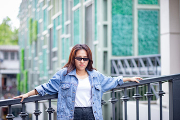 Portrait of Hipster Asian woman in white t-shirt, jean jacket and black trousers with beautiful modern building in background