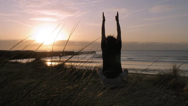 Practicing yoga and meditation on a beach at sunrise 4K
