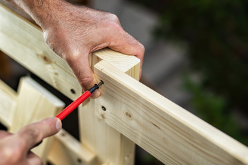 Adult carpenter craftsman with screwdriver screw the screw to fix the boards of a wooden fence. Housework do it yourself. Stock photography.
