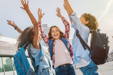 Happy children with hands up standing near school outdoors