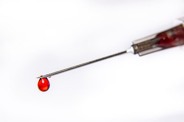 A syringe dripping a red blood like fluid isolated against a pure white background