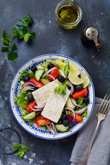Traditional Greek Salad. Vegetarian dish with fresh lettuce, olives, peppers, cucumbers, onions and feta cheese. On dark rustic concrete background. Top view.