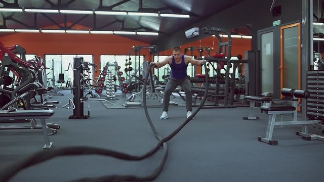 Athletic man training with ropes at the gym. High-intensity interval training. Slow motion