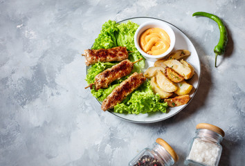 Grilled shish kebab served with fried potatoes and sauce on concrete background