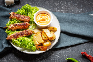 Grilled shish kebab served with fried potatoes and sauce on stone background
