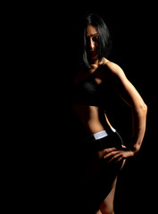 Adult girl with a sports figure in black bra and black shorts standing on a dark background