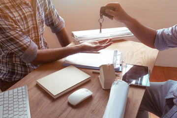 Happy men have been given the keys of their new home. Closeup from the hands of a real estate agent who gives a home key to a woman while her boyfriend signs a contract.