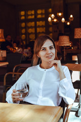 Beautiful girl sits in a cafe and drinks water.