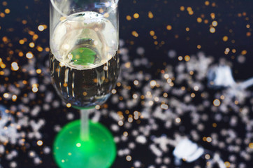 Neon glass with champagne on a black background with silver confetti.