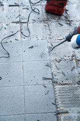 construction worker using a handheld demolition hammer and wall breaker to chip away and remove old floor tiles during renovation work