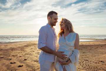 Love, wait for the baby. Portrait of a beautiful couple in white kissing on the background of the sunset sea.