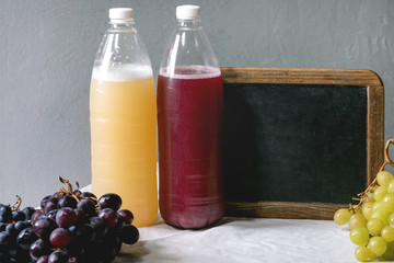 Traditional New european low alcohol red and white wine Federweisser, Neuer Wein, Burcak, Vin bourru in plastic bottles with black and green grapes on white table cloth. Empty chalkboard with space.
