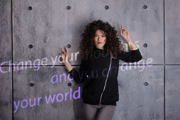 Curly woman actively posing on a wall background with colored light sign Change your thoughts and...