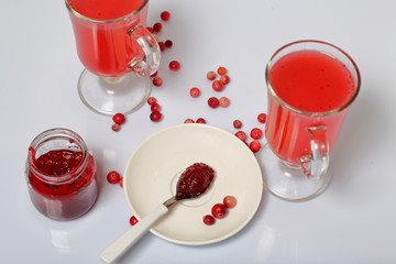 Homemade blanks. Cranberry jam in an open jar and glasses with cranberry juice. On a saucer is a teaspoon with jam. Several berries are scattered on the surface.