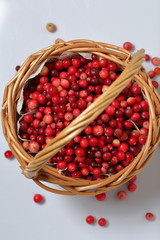 Basket filled with cranberries. It stands on a surface covered with linen cloth. Several berries are scattered on the surface.