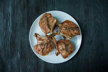Grilled steaks from pork ribs with spices and herbs. View of the super Dark wooden background.