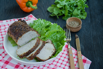 Baked pork tenderloin in spices sliced on a white plate with green salad. Dark wooden background.