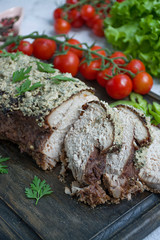 Baked pork chopped in a walnut and mint sauce on a cutting board with fresh herbs and vegetables. Light background.