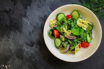 italian pasta salad farfalle, vegetables, mix leaves (tomato, cucumber, onion, lettuce, chard, arugula and more) menu concept. food background. copy space. Top view