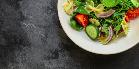 italian pasta salad farfalle, vegetables, mix leaves (tomato, cucumber, onion, lettuce, chard, arugula and more) menu concept. food background. copy space. Top view