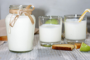 Bottle and glasses with refreshing fresh kefir on a light table with cracker and apple. Selective focus, focus on the bottle