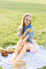 cute cute young girl holding a glass of juice and sitting on a blanket, summer picnic