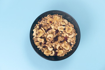 A fresh granola with dried and candied nuts and fruits in black bowl on blue bakground.