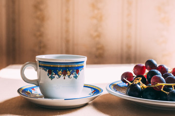 Cup of coffee on the table with grapes on the plate. Retro, ceramic cup