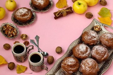 Homemade muffins with apples and nuts and two cups of coffee arranged on a pink background, top view, Copy space, Autumn composition, horizontal orientation