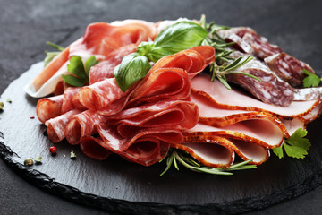 Marble cutting board with prosciutto, bacon, salami and sausages on wooden background. Rustic Meat platter
