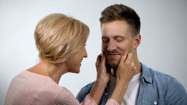 Mum Pinching Adult Son Cheeks, Male Smiling, Overprotection Effect Concept