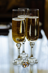 Two glasses of sparkling champagne with wedding rings on glossy table