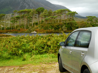 Small rented car parked in Connemara National park, Pine Island in the background out of focus, Concept travel and discover Ireland.