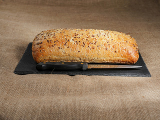Uncut sourdough bread with nuts on a slate plate with a knife, Rustic hessian surface.