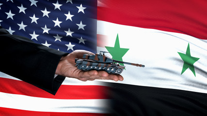 Official hand holding toy tank against USA and Syria flags, military forces