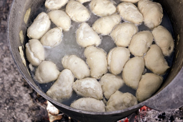 Dumplings are boiling in cauldron. Preparation of Ukrainian traditional dish on fire.