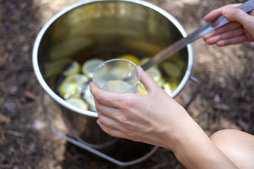 Homemade lemonade in a bucket with a slices of lemon. Close up photo of pouring a lemonade in a plastic cup in the forest.