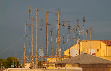 Cluster of old and rusty TV antennas on a building's rooftop beautifully lit by the setting sun...