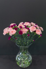 A large bouquet of red and pink carnations in a transparent glass vase on a dark background