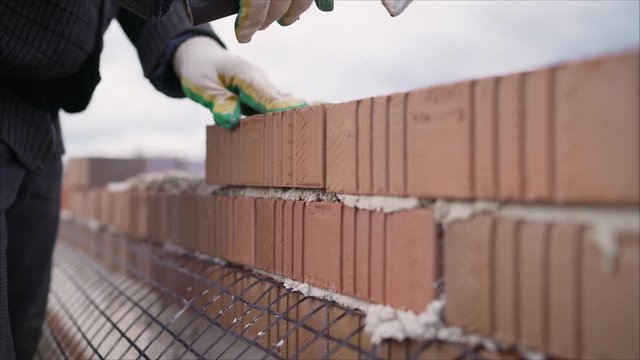 Bricklayer working in construction site of a brick wall. Bricklayer putting down another row of bricks in site. Worker puts a brick wall