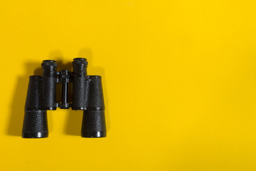 Black metalic binoculars on a yellow background