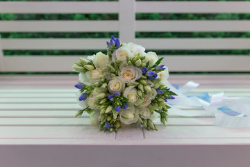 Sensual bright bouquet of fresh flowers with ribbons on the background of a white bench (Flowers: rose, Eustoma. Primary colors: white, blue)