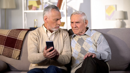 Elderly males holding smartphone sitting home sofa, online internet connection