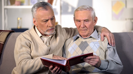 Elderly male friends watching album photos together, family memories, past