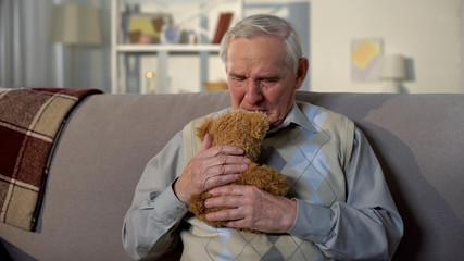 Crying elderly man hugging teddy bear, missing grandchildren, family support
